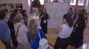 Participants of the HSC Rountable in Mexico stand gathered around a whiteboard while one participant is speaking to them. 